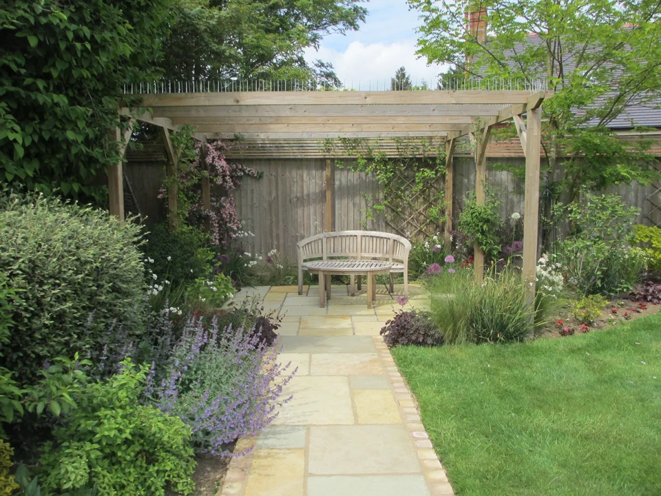 A well-kept Cotswold garden maintained by George-Stone Gardens — pergola, planted borders and crisp lawn edges